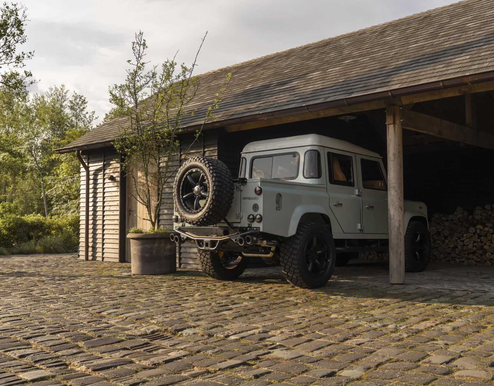 Sage-green bespoke Defender parked beside a barn