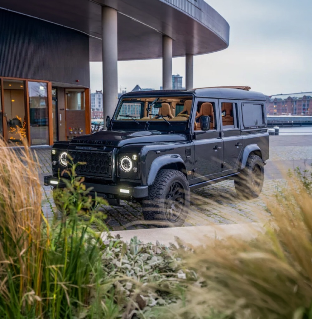 Black Defender EV parked outside a waterfront building