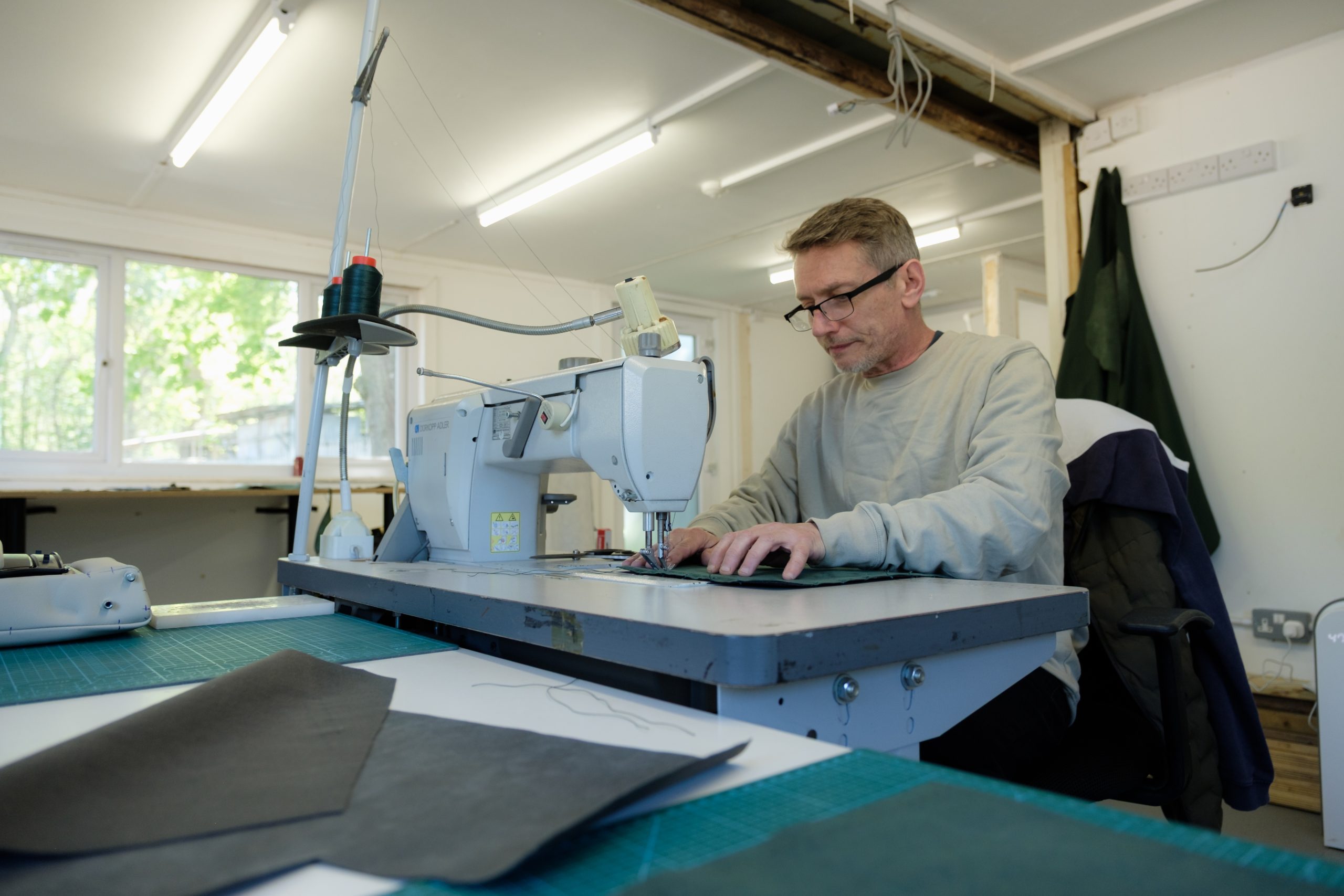 Craftsman hand-stitching a leather panel on an industrial sewing machine