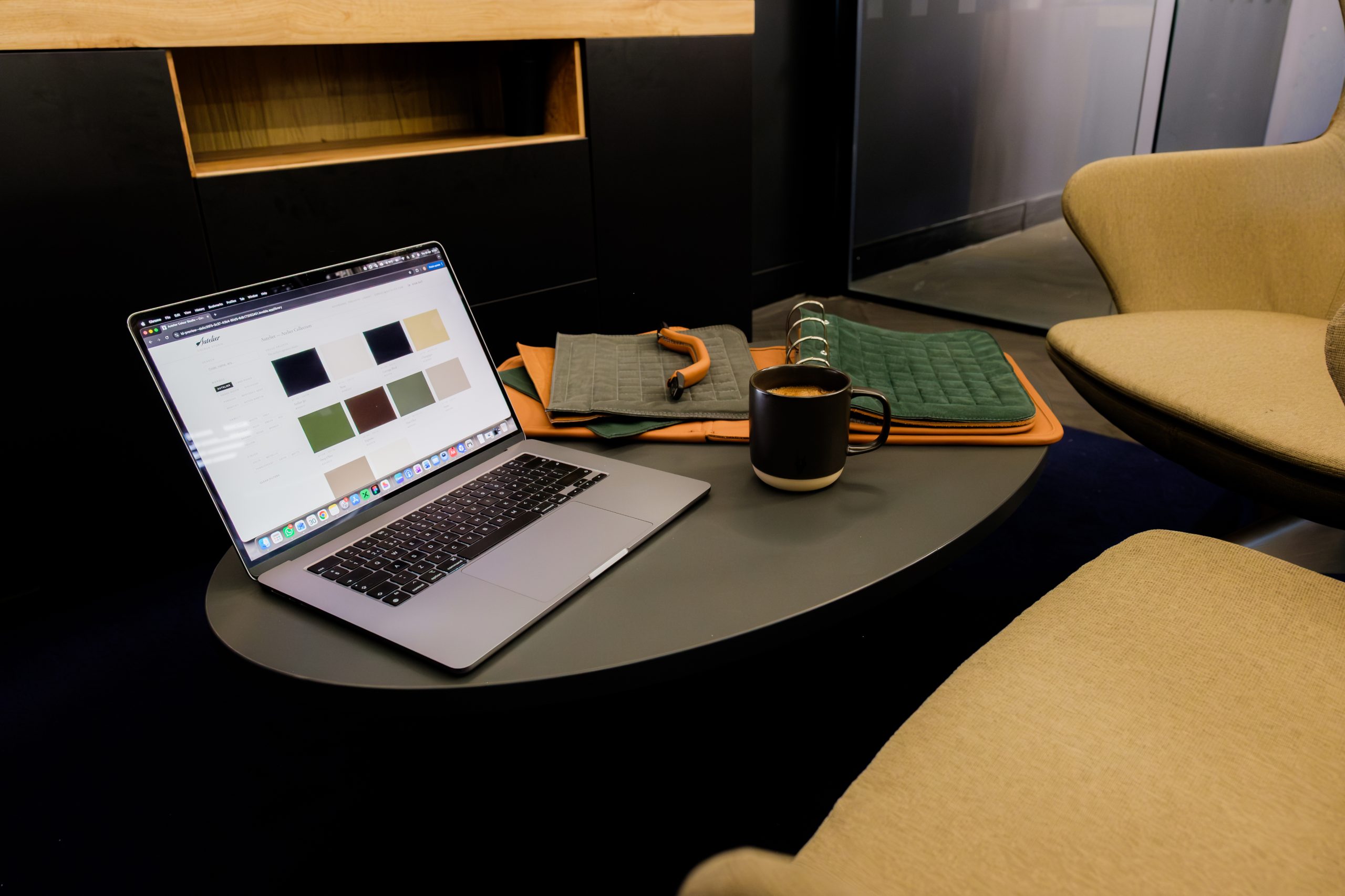 Laptop showing material swatches on a workshop desk beside a rolled leather sample book