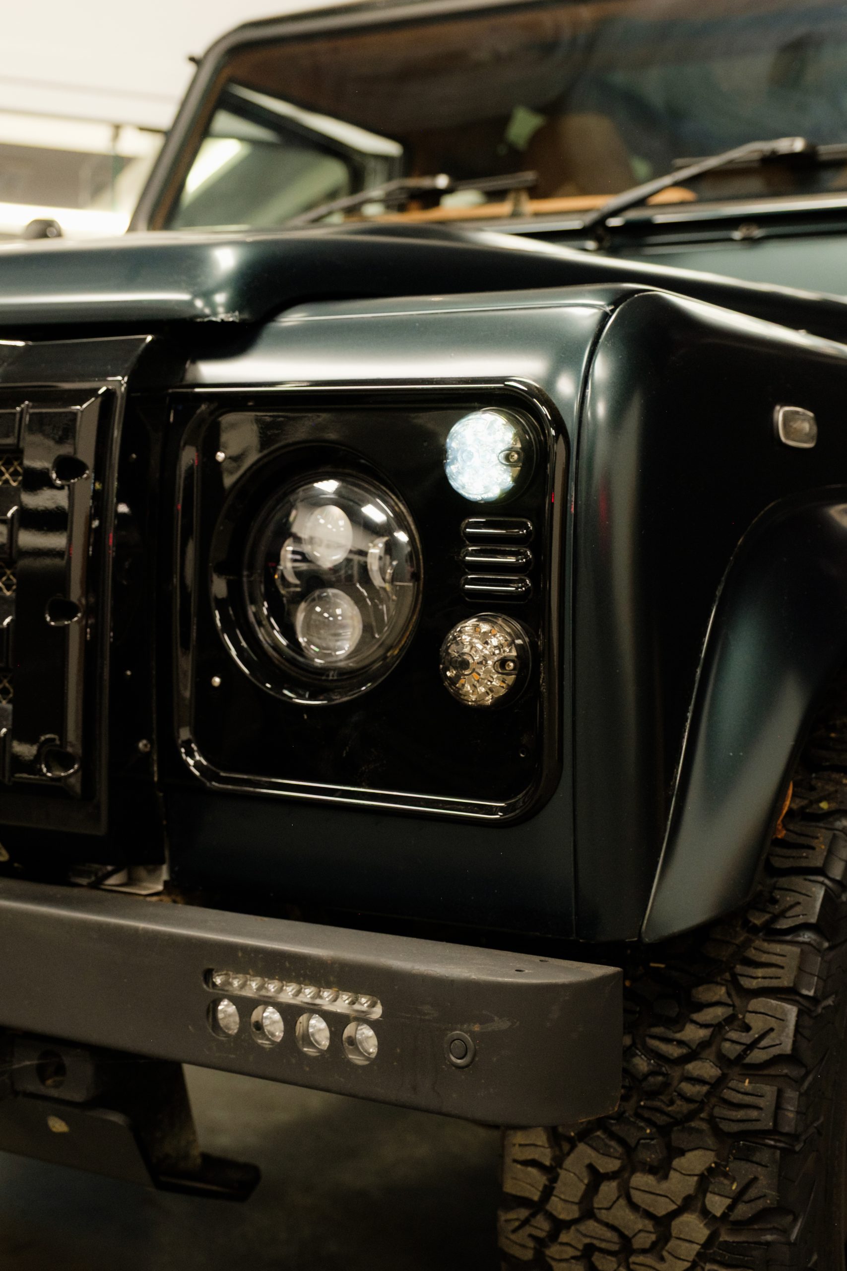 Close-up of a dark green Defender's bonnet and headlight in a workshop