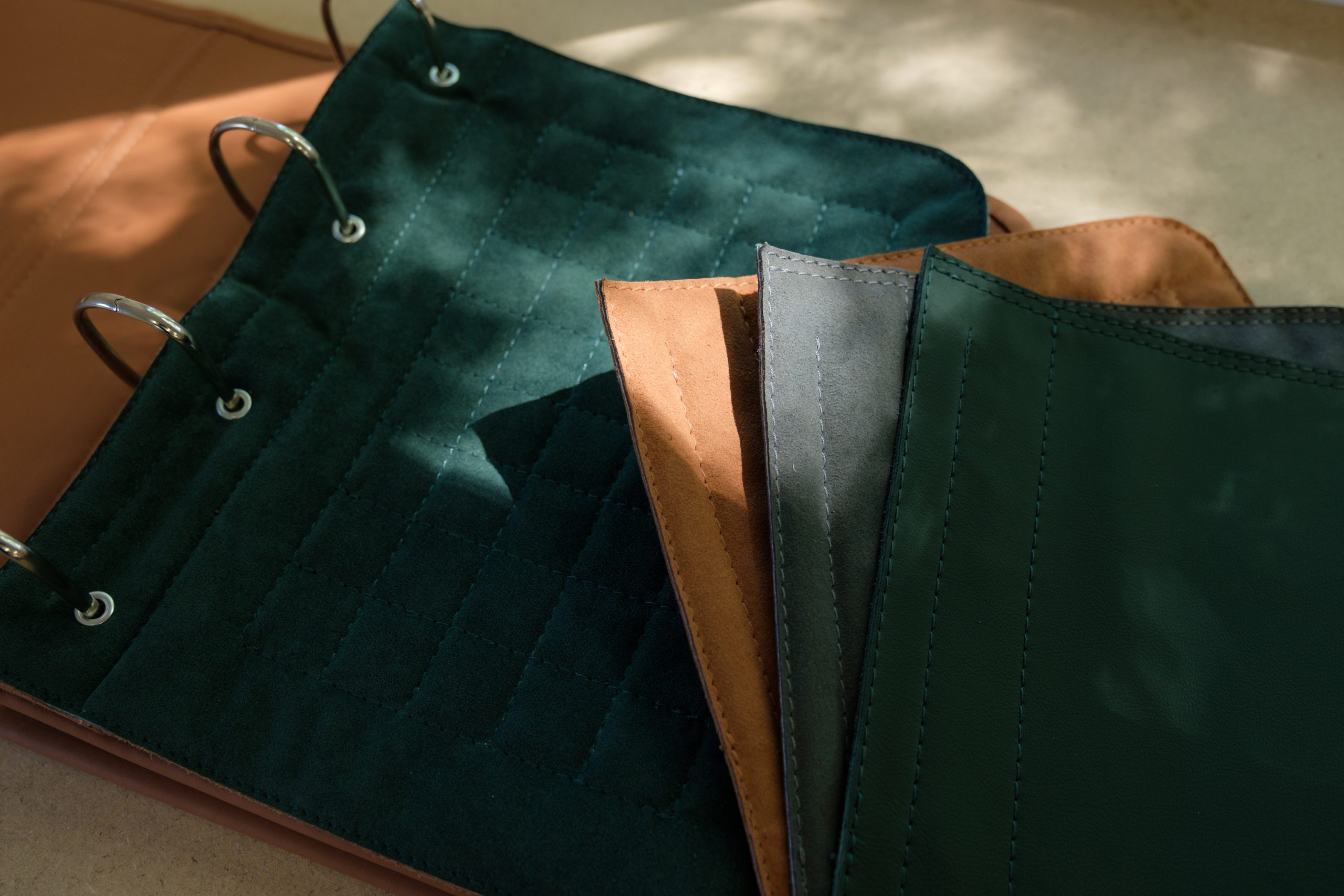 Quilted forest-green leather trim book open beside fanned tan, grey and green material swatches